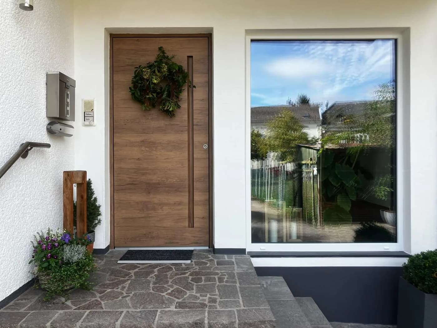 Haustür AGE 1030 in heller Eichen-Holzoptik mit langem Stangengriff, daneben ein großes Fenster