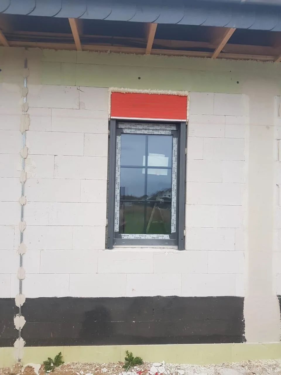 Anthrazitgraues Fenster mit Sprossen im Scheibenzwischenraum in einem Rohbau, darüber der Rollladenkasten
