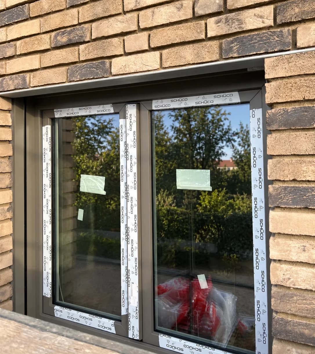 Zweiflügeliges Kunststofffenster mit Stulp ohne Mittelpfosten in einer Klinkerfassade, noch mit Schüco-Schutzfolie